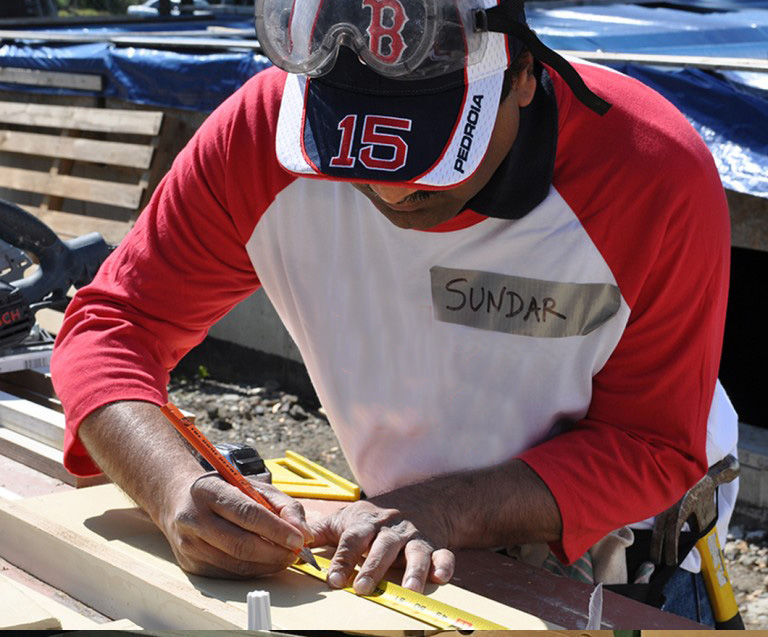 Sundar, a Seed4equityer using a tape measure while volunterring in his BBH Cares t-shirt and Red Sox hat with safety goggles on his head. 